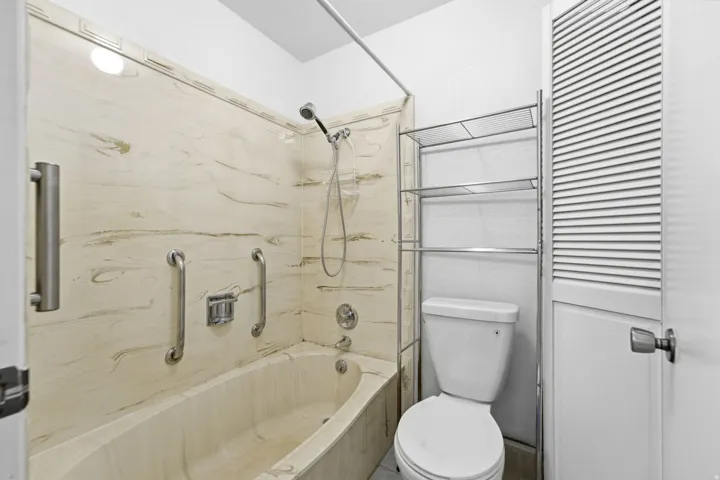 Bathroom featuring a built-in tub with tile surround, a shower with a handheld fixture, and a louvered door
