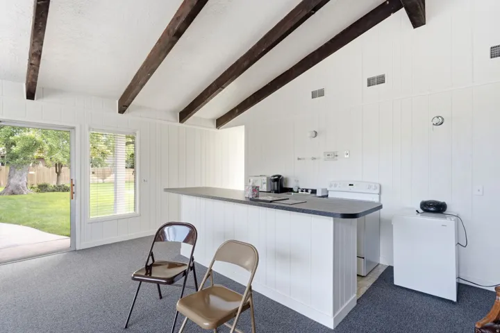 Vaulted ceiling with exposed wood beams, white paneled walls, a breakfast bar with countertop, a built-in range, and direct access to a rear patio and lawn