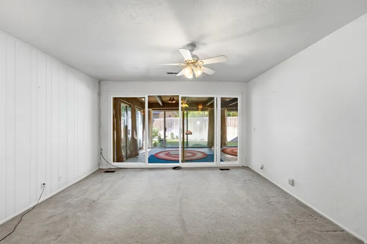 Carpeted flooring, white paneled wall, ceiling fan with light fixture, and sliding glass doors