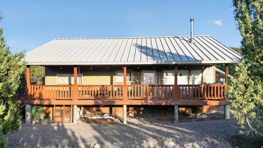 Expansive front porch with wooden railings, a light gray metal roof, and a visible chimney