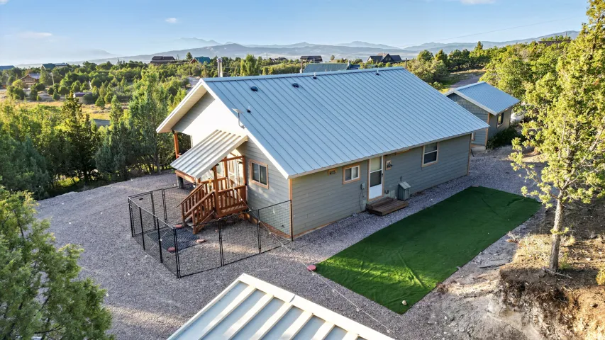 Light gray siding with a metal roof, featuring a covered wood deck and a fenced area