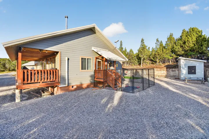 Gravel-covered lot featuring a shed, an enclosed outdoor area, and a covered porch with wood railings