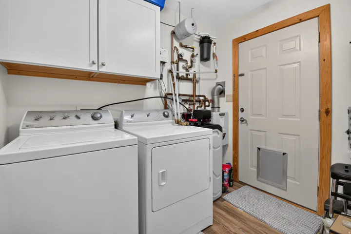 White upper cabinetry, wood-finish flooring, and utility access