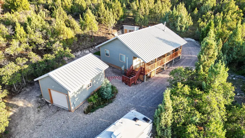 Main residence with a covered porch, detached garage, and gravel driveway, all surrounded by mature trees
