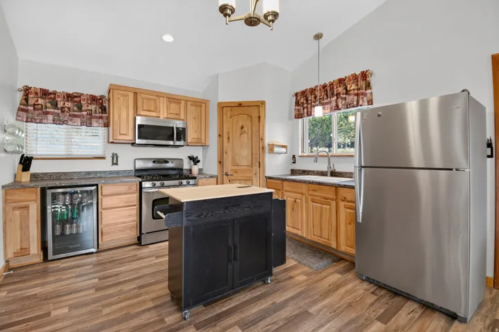 Stainless steel appliances, wood-finish flooring, light wood cabinetry, stone-look countertops, and a portable kitchen island