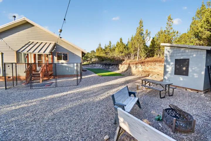 Gravel outdoor area featuring a fire pit, two benches, and a picnic table