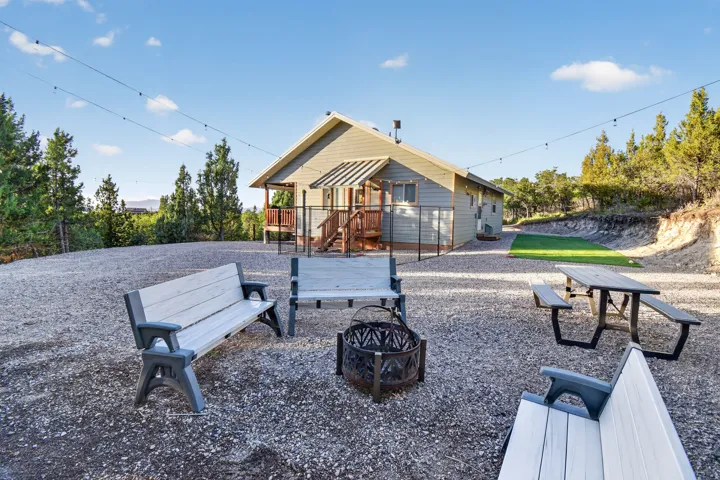 Gravel outdoor area with a fire pit, string lighting, and a fenced perimeter