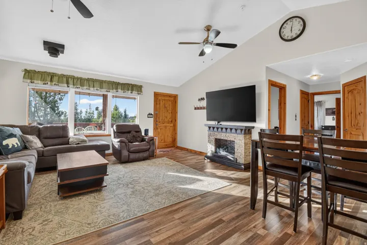 Vaulted ceiling with dual ceiling fans, wood-finish flooring, stone-accented fireplace, wood interior doors, and multiple large windows