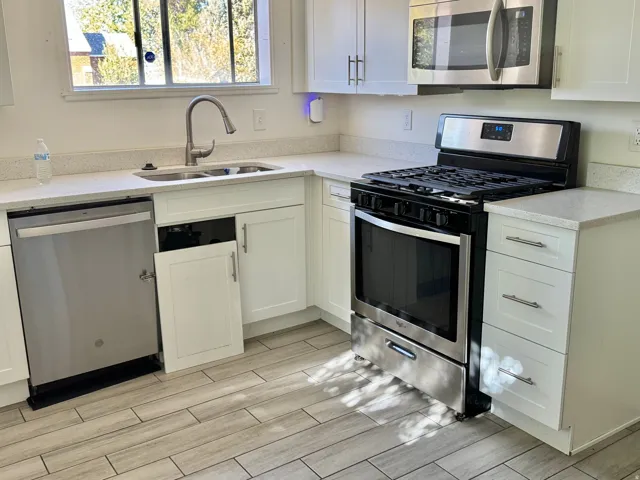 Stainless steel appliances, white cabinetry, light-toned countertops, and wood-finish tile flooring