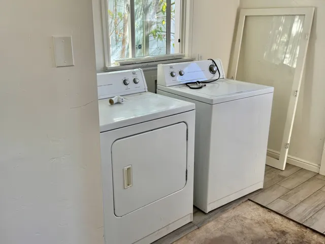 White dryer and washing machine with a window above, set against light-toned plank flooring