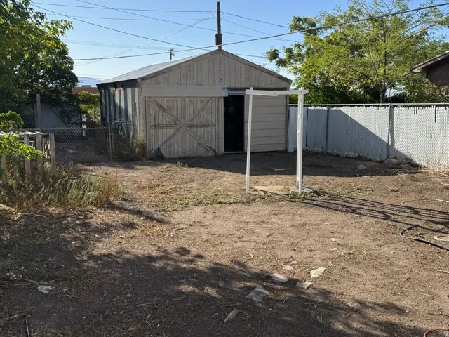 Detached shed with double barn doors, chain link fencing, and an expansive yard space