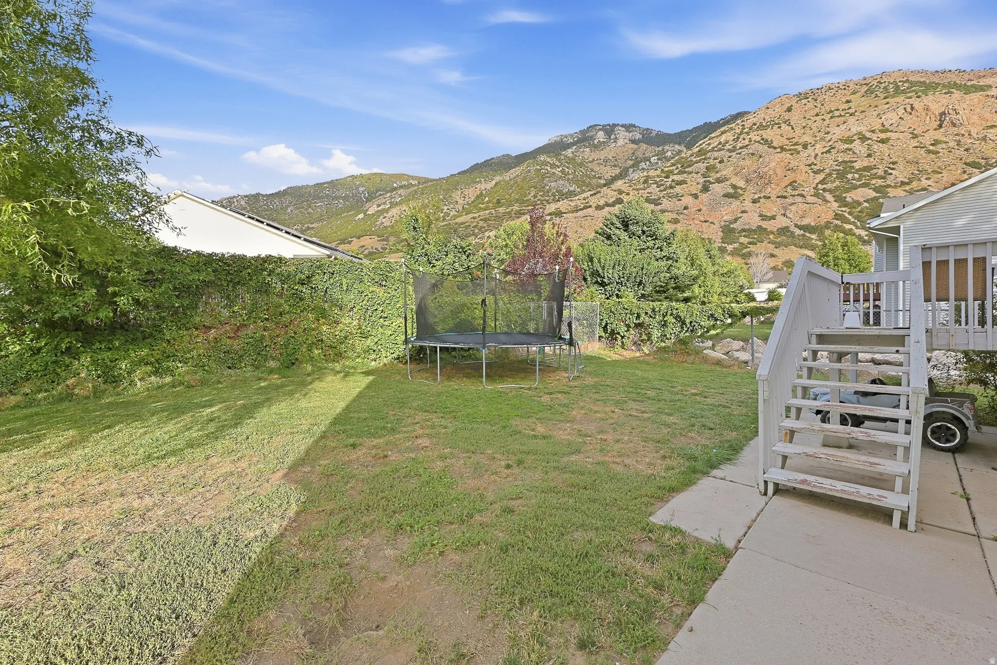 Rear yard with a lush green lawn, concrete patio, and a multi-level deck