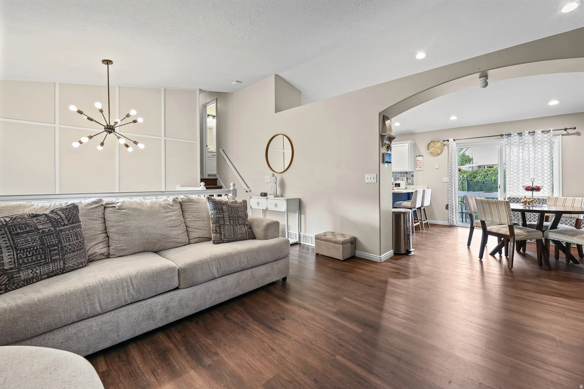 Open-concept living area featuring wood-finish flooring, a contemporary chandelier, and an arched doorway