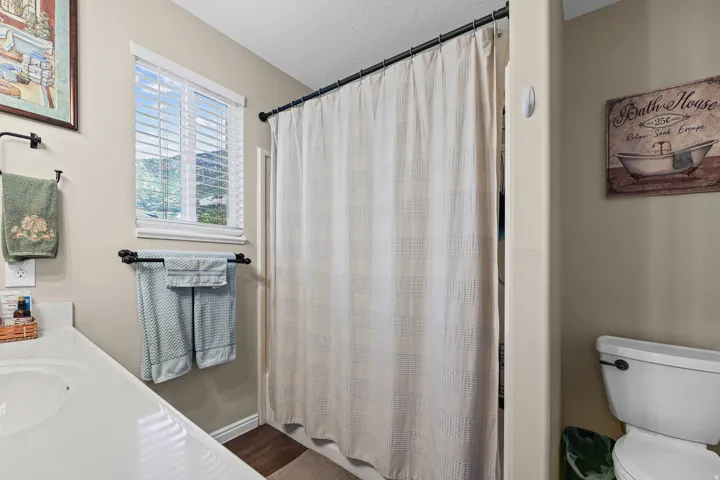 Bathroom featuring a white vanity with integrated sink, white window blinds, a shower enclosure with a curtain rod, and a white toilet