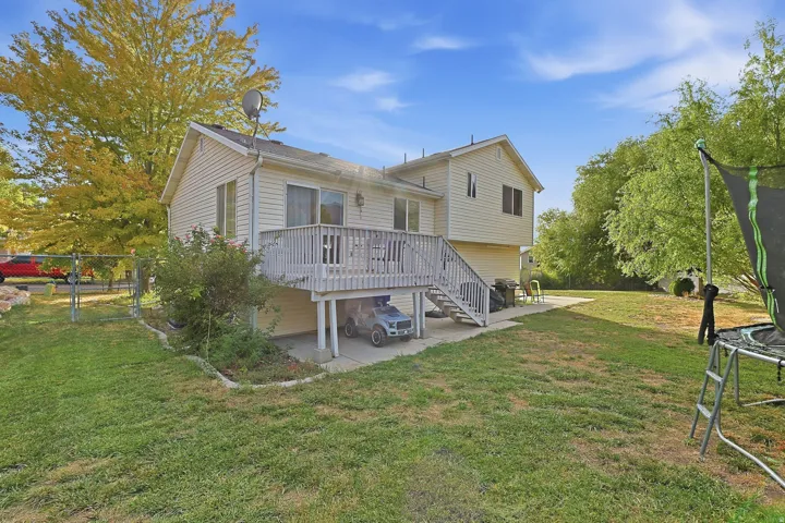 Rear exterior with light-colored siding, a wooden deck, and a spacious grassy area