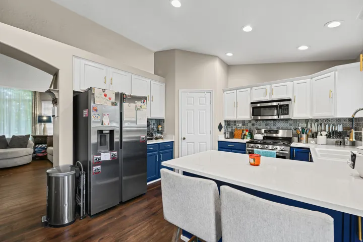 Kitchen featuring a large central island with a white countertop, two-tone cabinetry with gold-finish hardware, stainless steel appliances, and wood-finish flooring