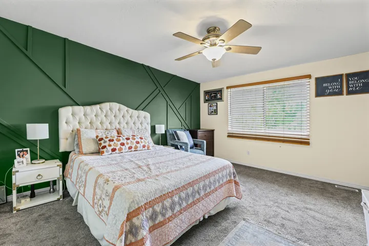 Feature wall with geometric paneling, ceiling fan with light fixture, window with blinds, and neutral carpeting