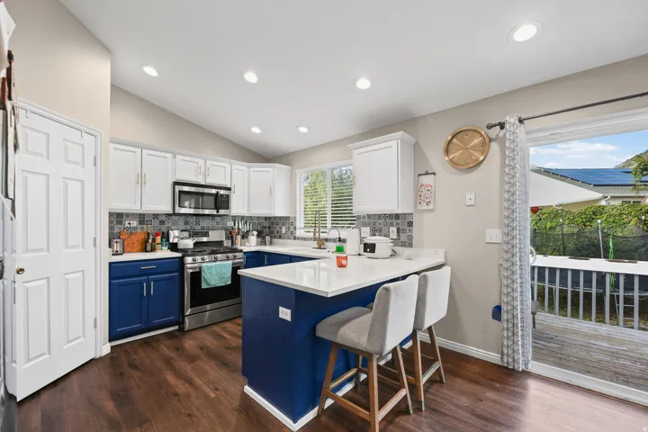 Kitchen featuring vaulted ceilings, wood-finish flooring, stainless steel appliances, a white countertop island, and sliding glass door access to an exterior deck
