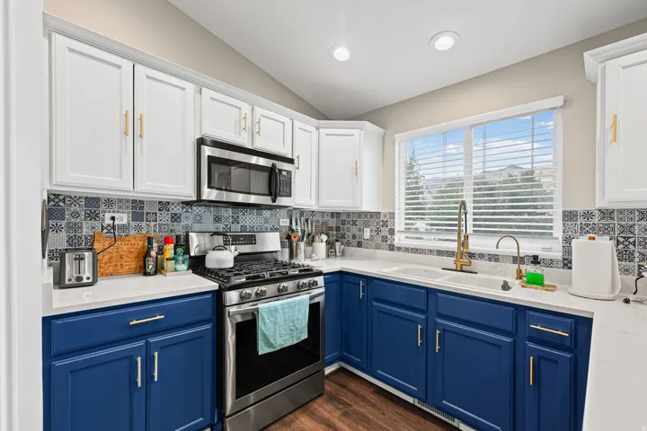 White upper cabinetry, blue lower cabinetry, stainless steel appliances, patterned tile backsplash, and recessed lighting