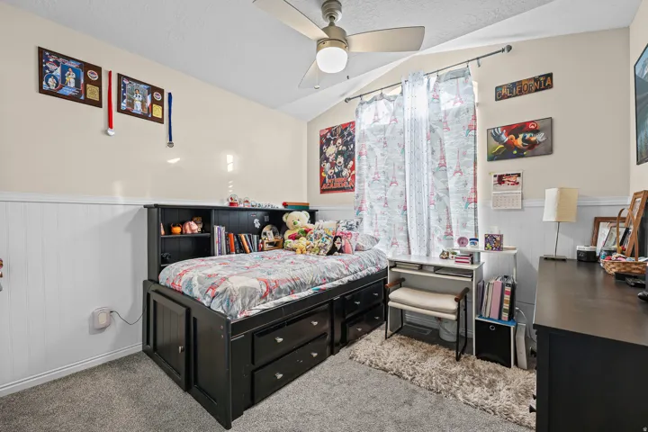 Carpeted bedroom featuring a built-in bed frame with storage, a ceiling fan, and wainscoting