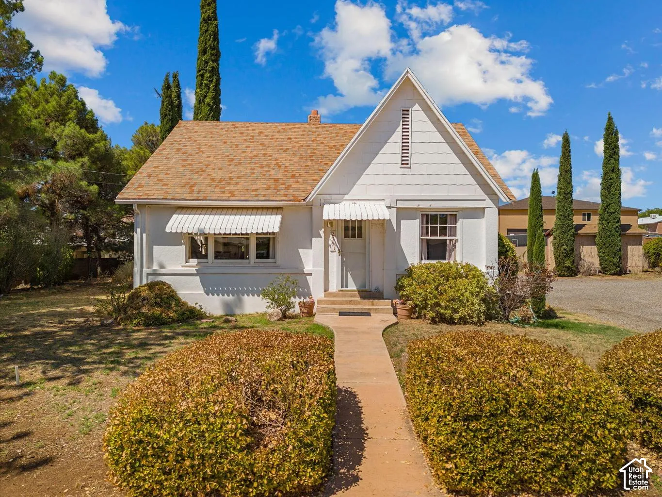 White exterior siding, peaked gable, covered entry, front walkway, and mature landscaping