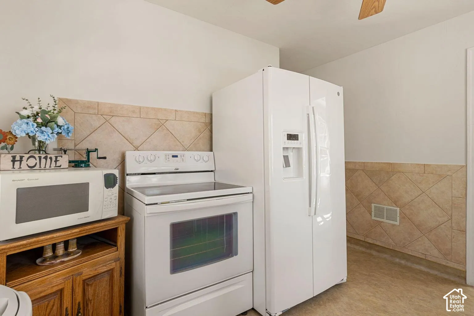 White freestanding electric range, white side-by-side refrigerator, and neutral tile wainscoting