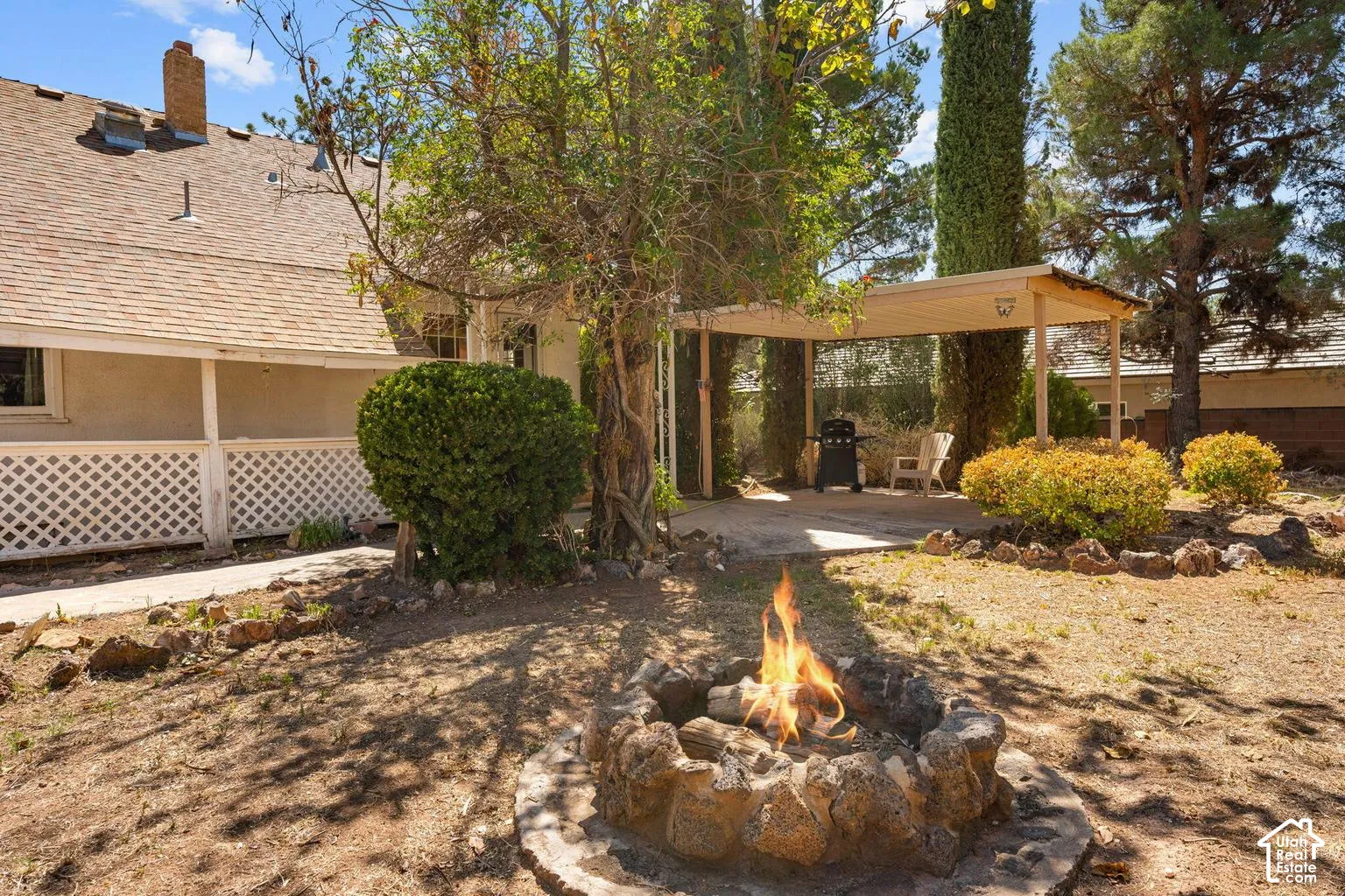 Spacious backyard featuring a stone fire pit, covered patio area, mature trees, and established landscaping