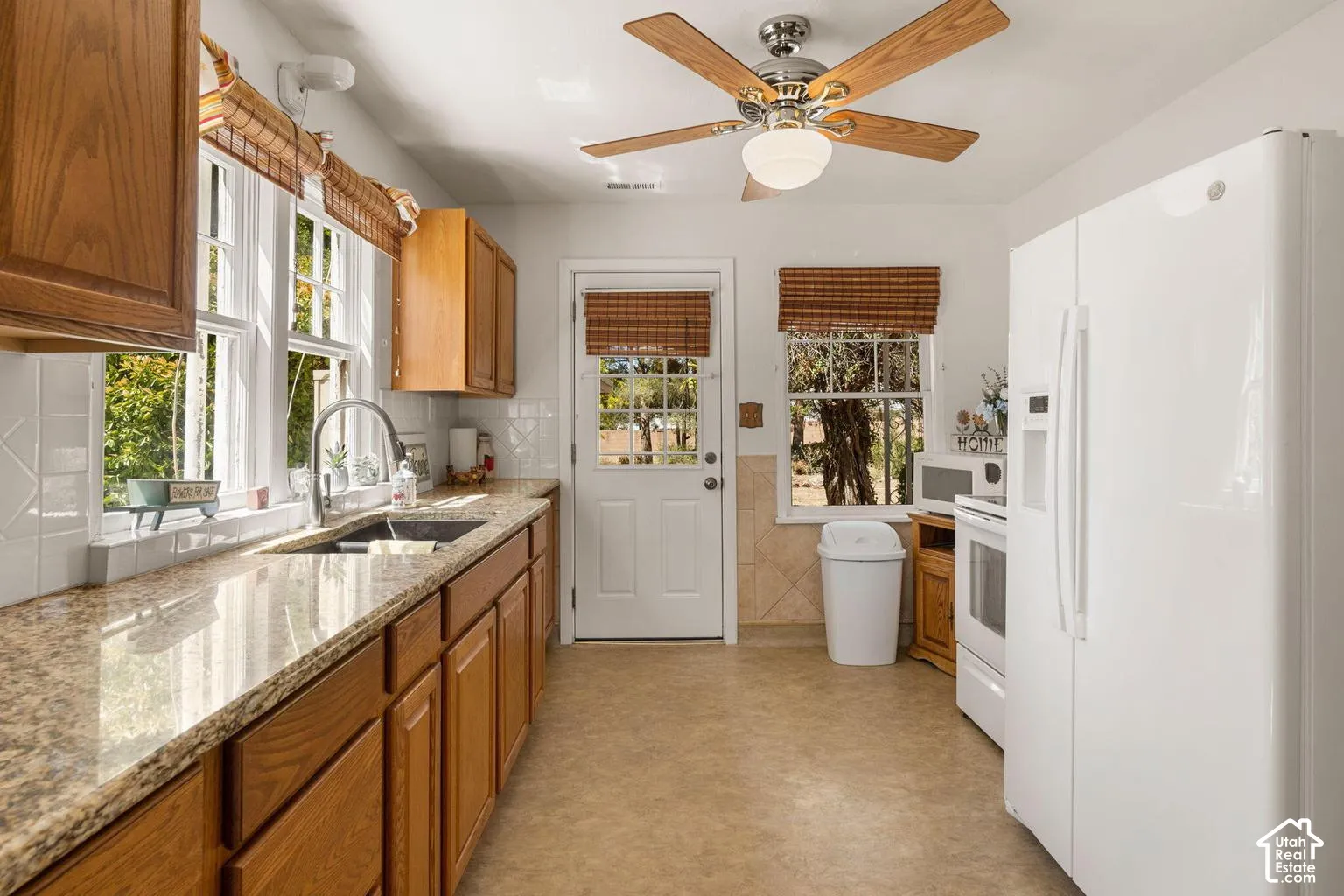 Kitchen featuring wood cabinetry, granite-finish countertops, subway tile backsplash, and a ceiling fan with integrated lighting