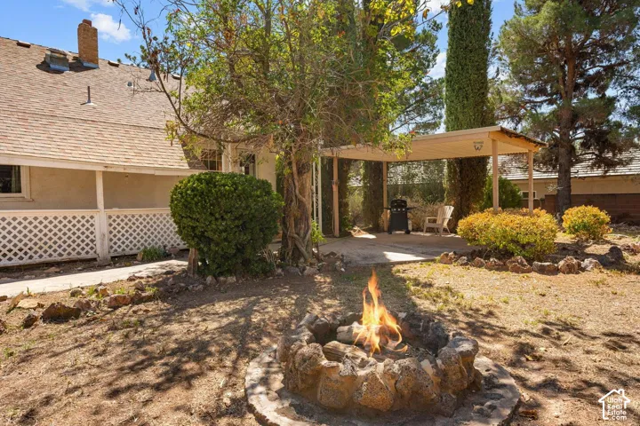 Spacious backyard featuring a stone fire pit, covered patio area, mature trees, and established landscaping