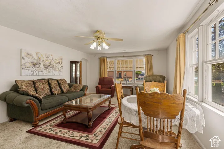 Living area with multiple windows, a ceiling fan with light fixture, and an arched doorway