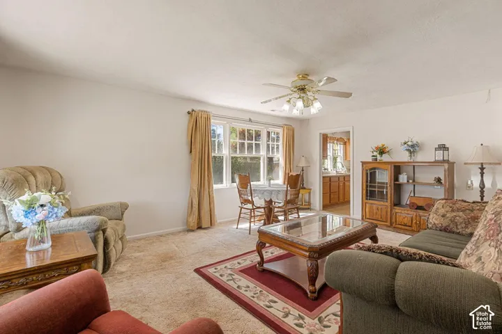 Carpeted living area with a ceiling fan, a window with natural light, and a framed opening to another room