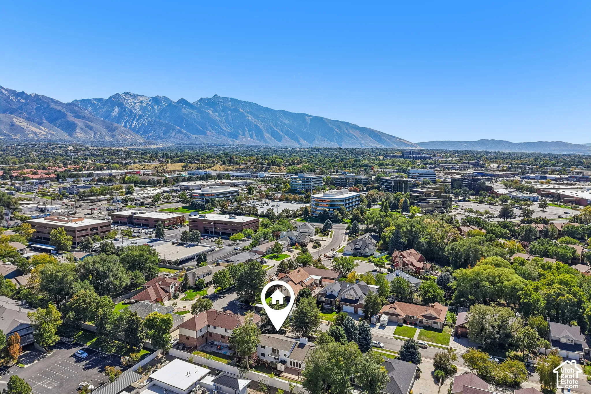 Mountain backdrop, residential neighborhood setting, mature trees, commercial buildings in the distance, clear sky