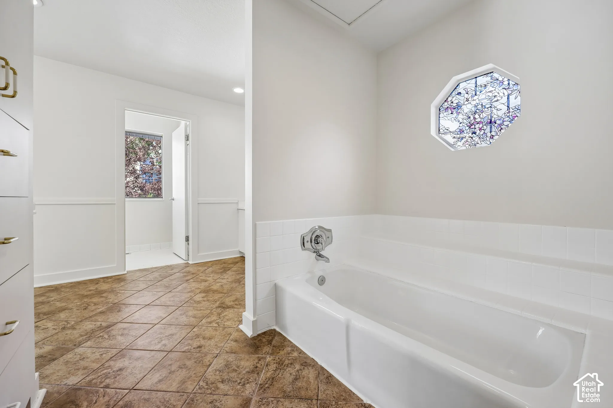 Built-in tub with chrome fixtures, octagonal window, white wainscoting, and tile flooring