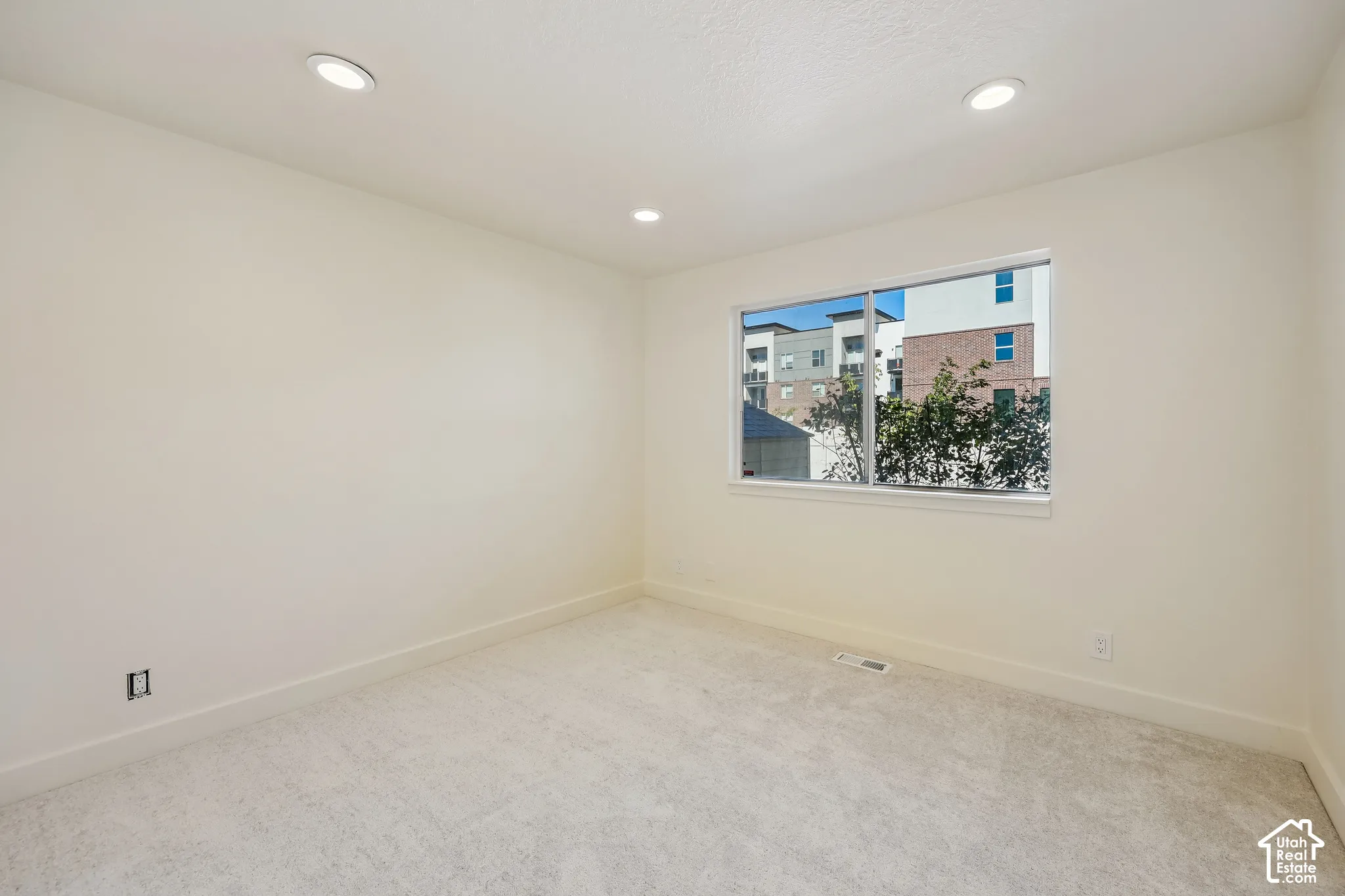 Recessed lighting, light-toned carpeting, and a window with white trim