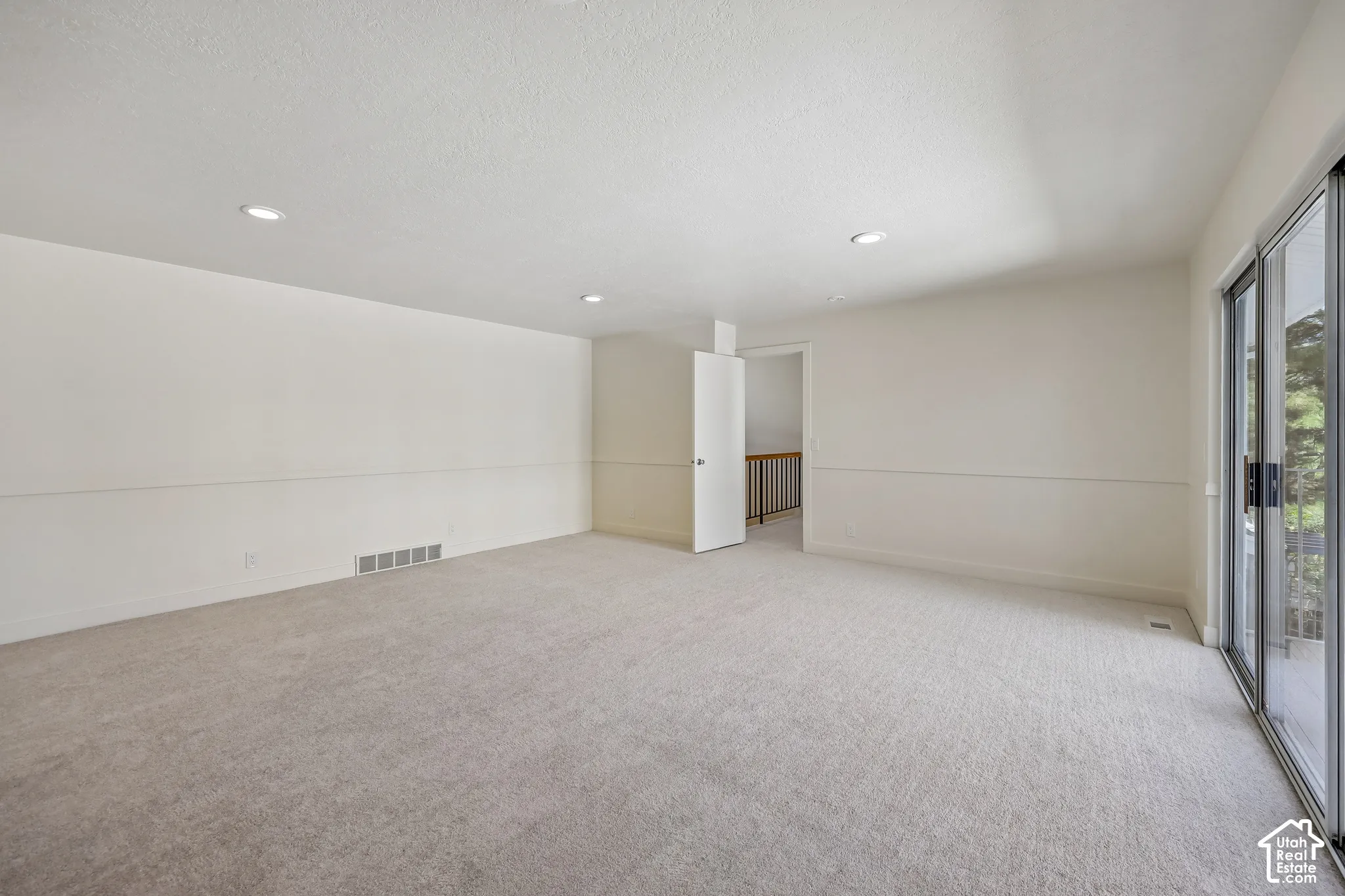 Spacious room with recessed lighting, light-toned carpeting, and a sliding glass door to an outdoor area