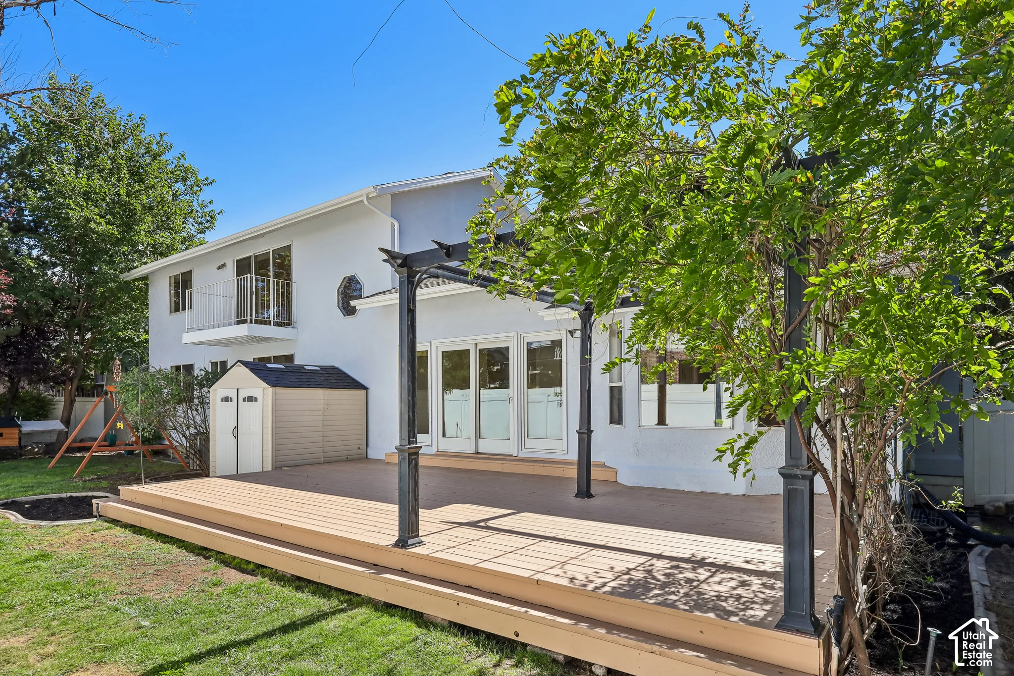 Expansive outdoor deck with a pergola, ground-level access, and a second-story balcony