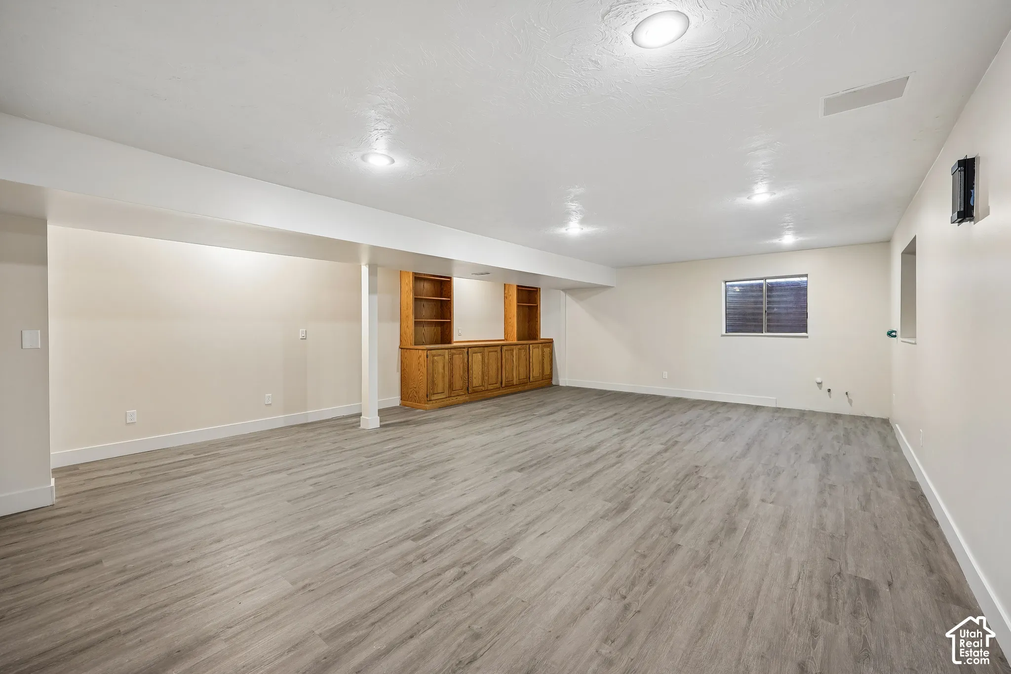 Recessed lighting, light-toned wood-finish flooring, built-in wooden cabinetry, and a window with horizontal blinds