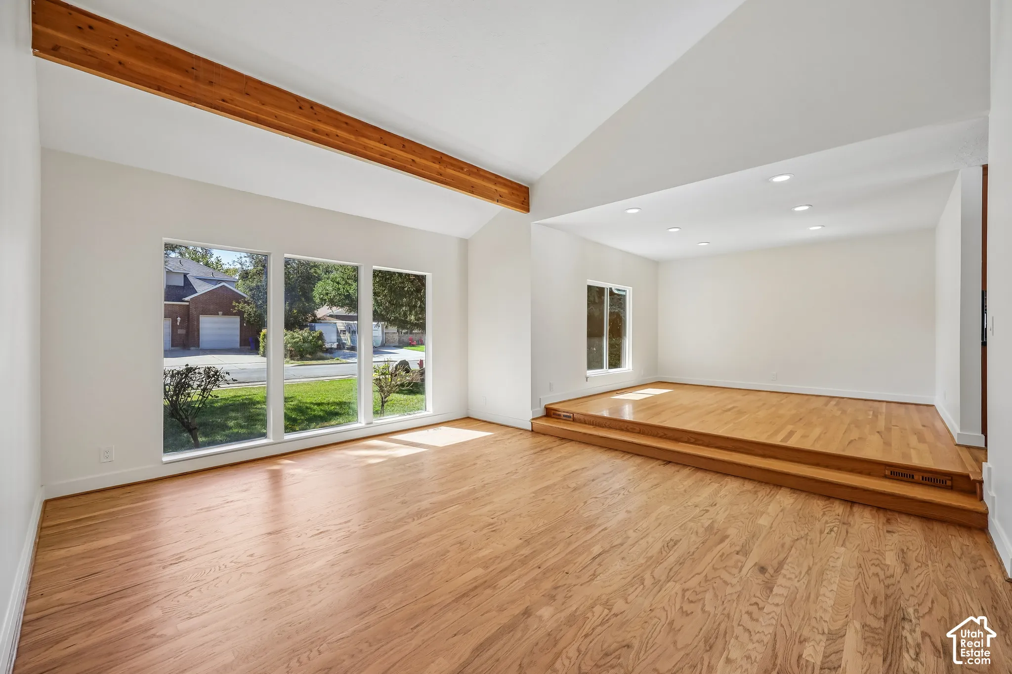 Vaulted ceilings with exposed wood beams, wood-finish flooring, recessed lighting, expansive windows, and a raised platform area