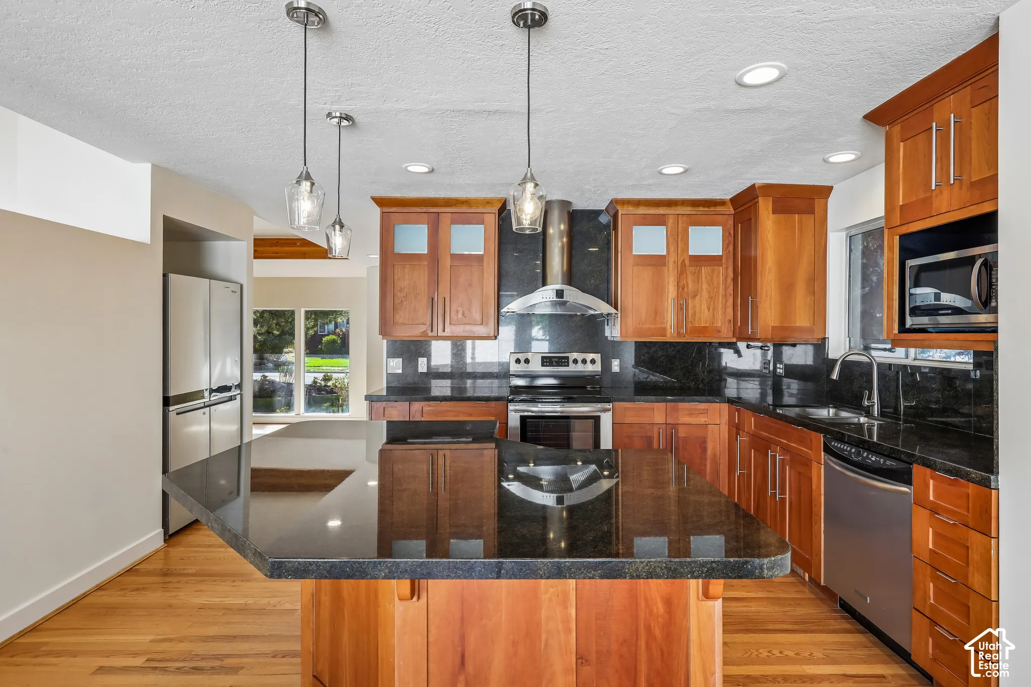 Kitchen featuring a large island with dark stone countertops, wood cabinetry, stainless steel appliances, and pendant lighting