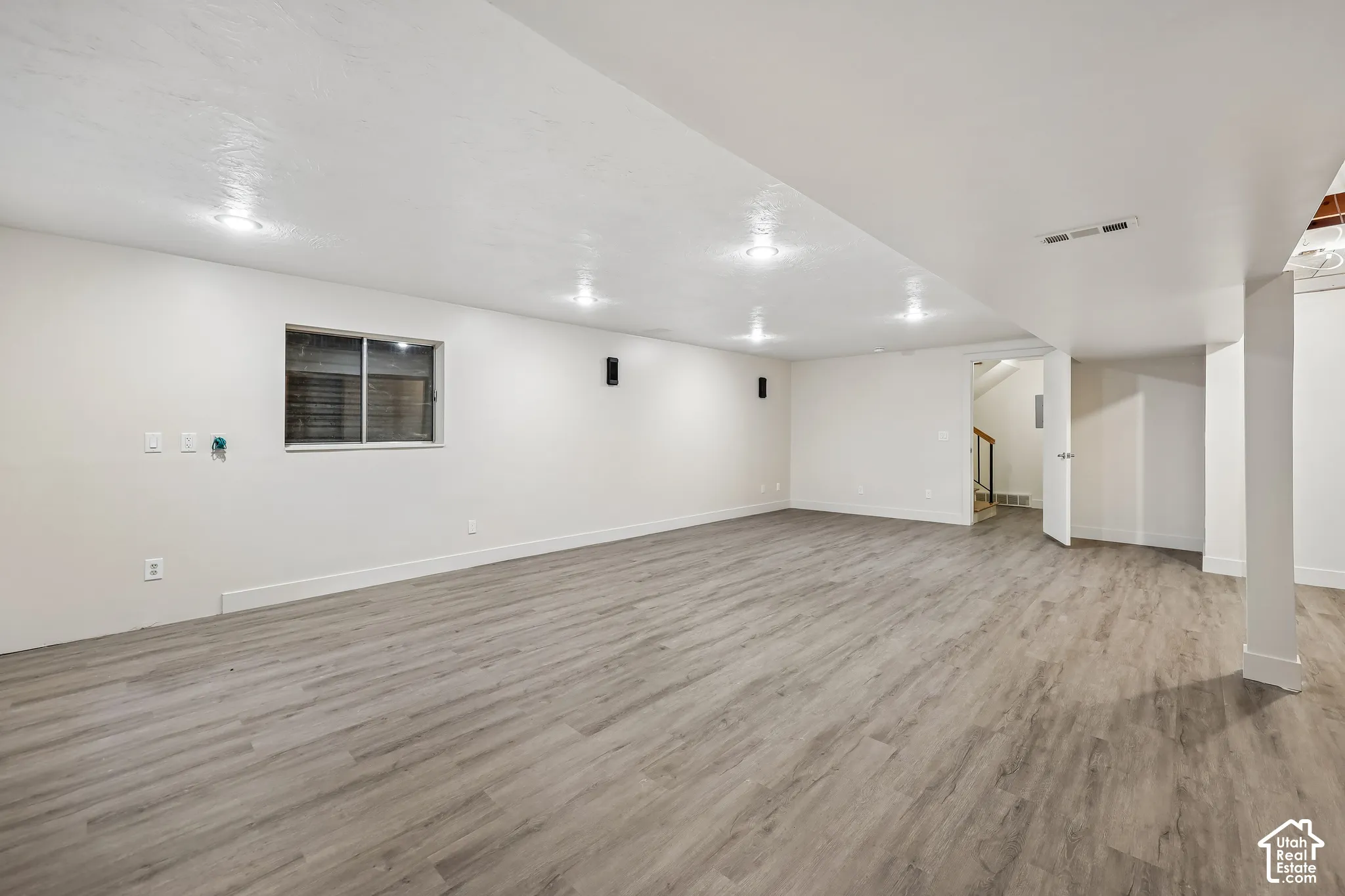Spacious room featuring wood-finish flooring, recessed lighting, and a white interior door