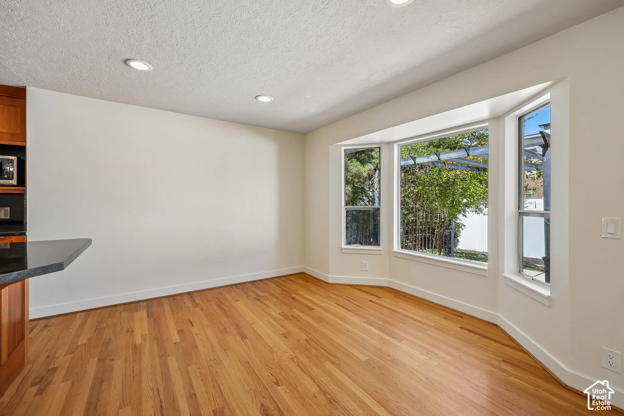 Hardwood flooring, recessed ceiling lighting, bay window, built-in wood cabinetry, and a dark countertop