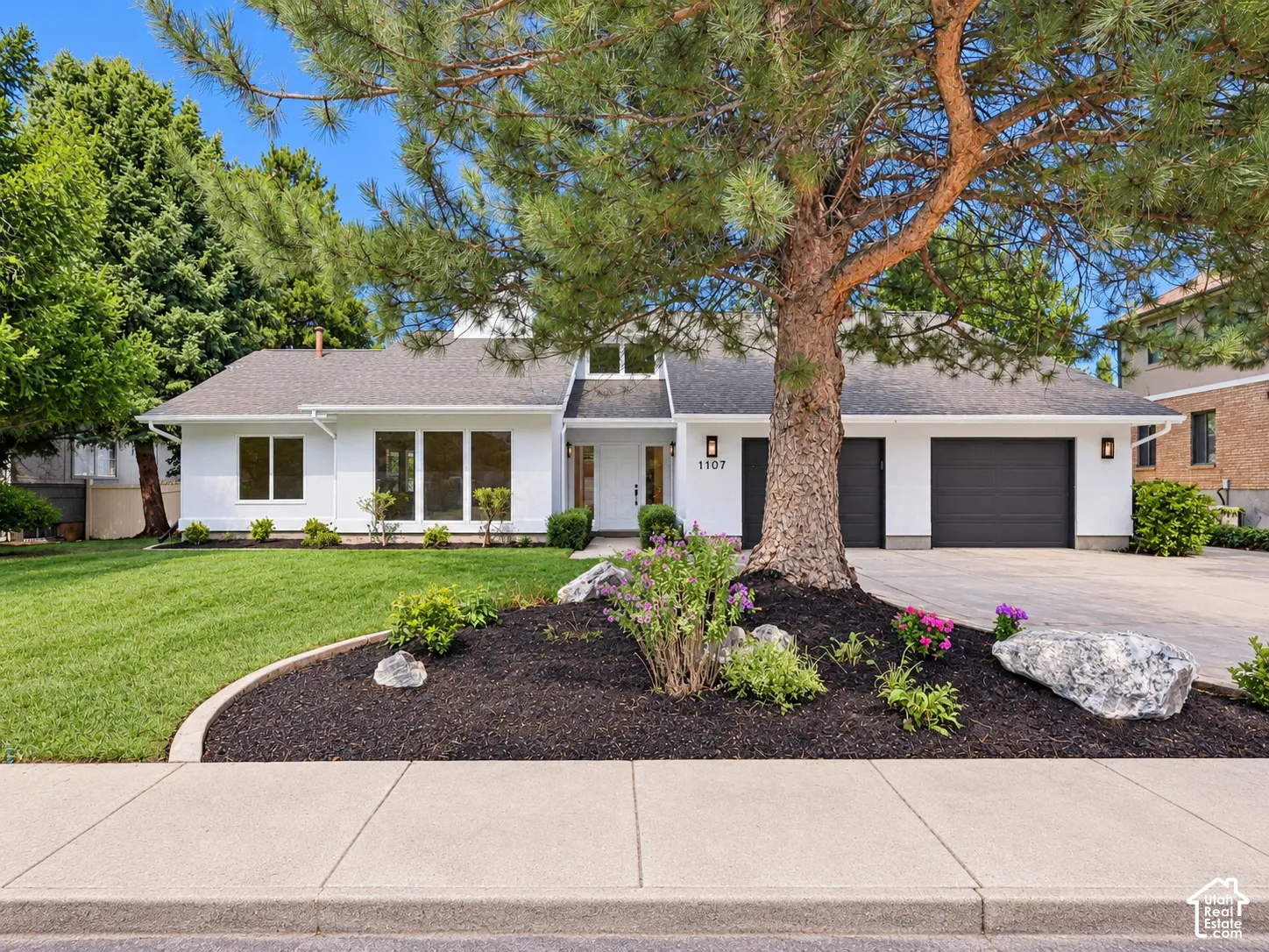 White exterior with dark-paneled garage doors, a paved driveway, and a well-maintained lawn