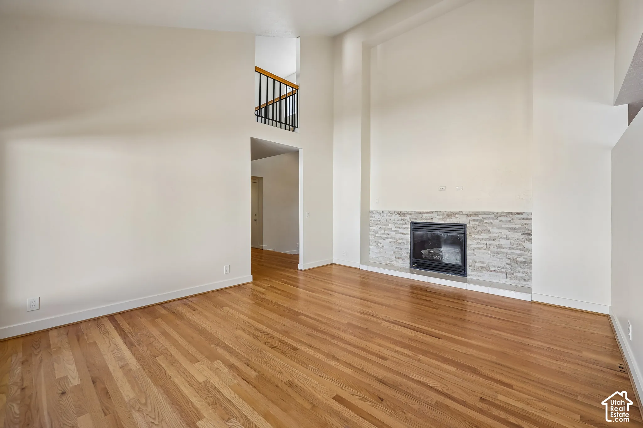 Hardwood flooring, fireplace with stacked stone surround, high ceilings, and an interior balcony with black metal railing