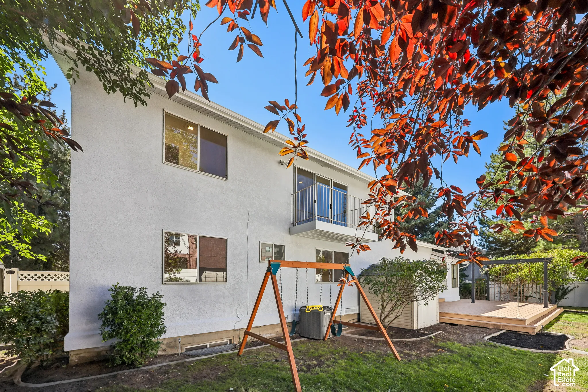 White stucco exterior with multiple windows, second-story balcony with metal railing, and a ground-level wood-deck with a metal pergola