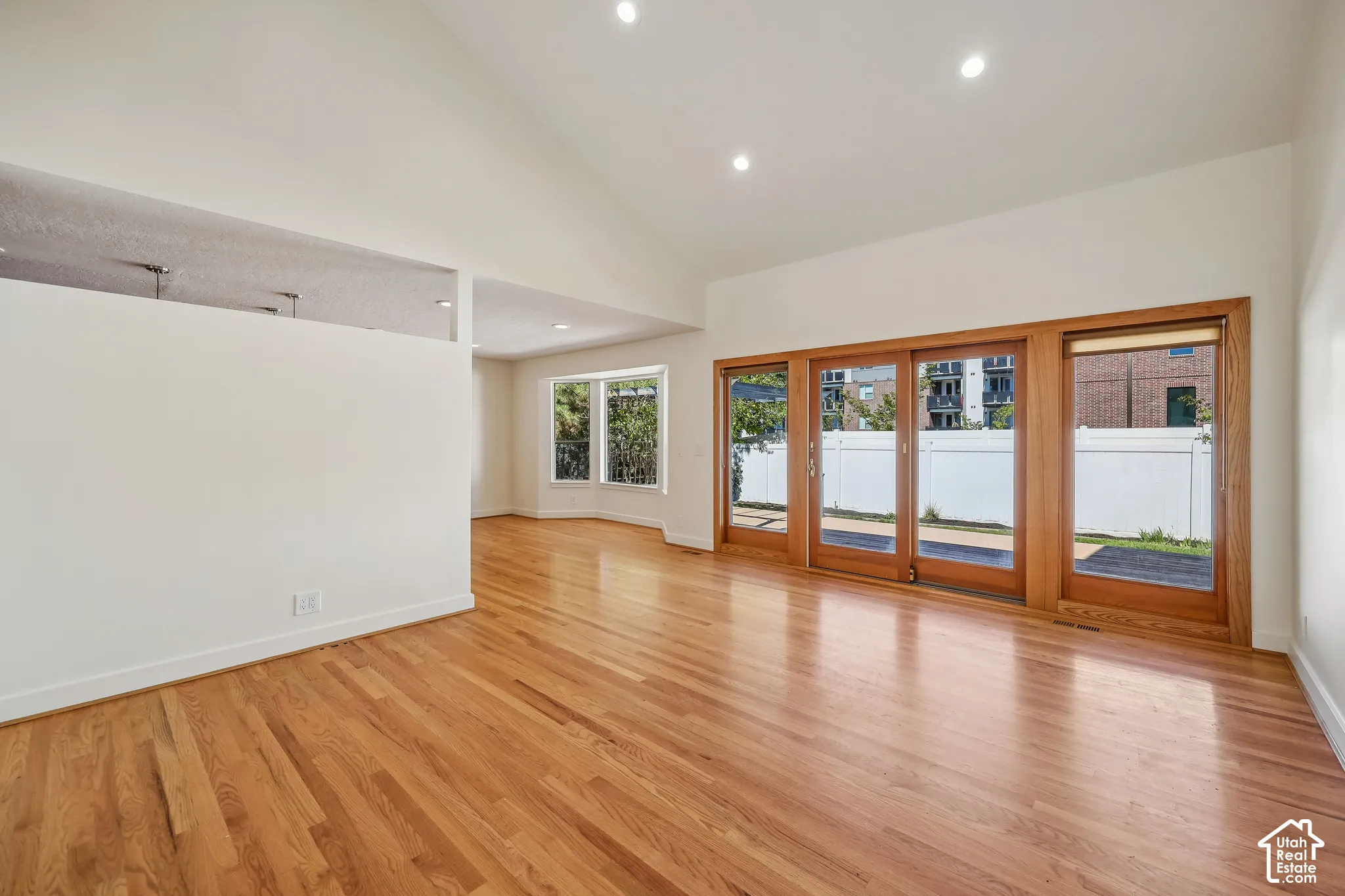 Hardwood flooring, vaulted ceiling, recessed lighting, expansive sliding glass doors with wood framing, and multiple windows