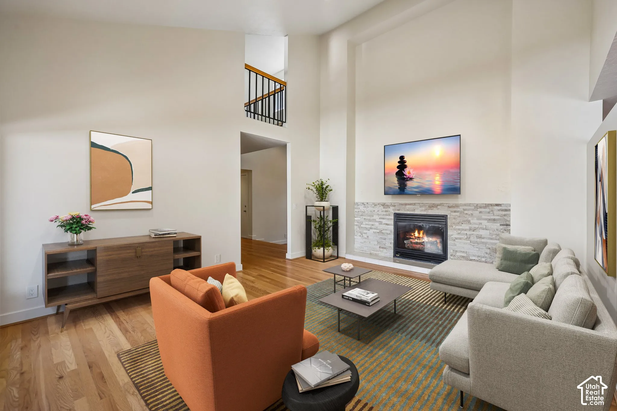 Two-story ceilings, a fireplace with a stacked stone surround, and wood-finish flooring