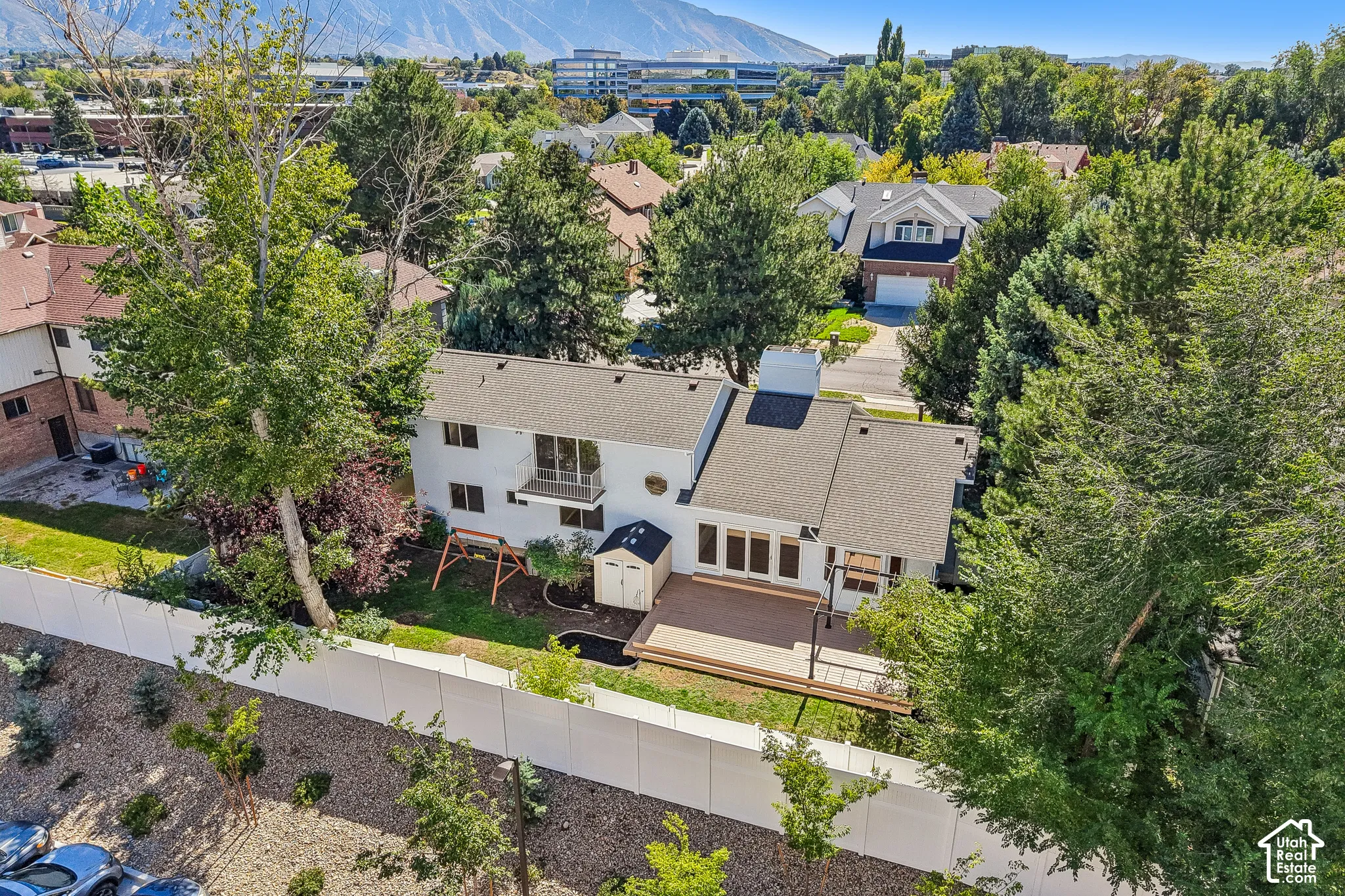 Expansive rear yard featuring a large wood-finish deck, mature trees, and a white privacy fence