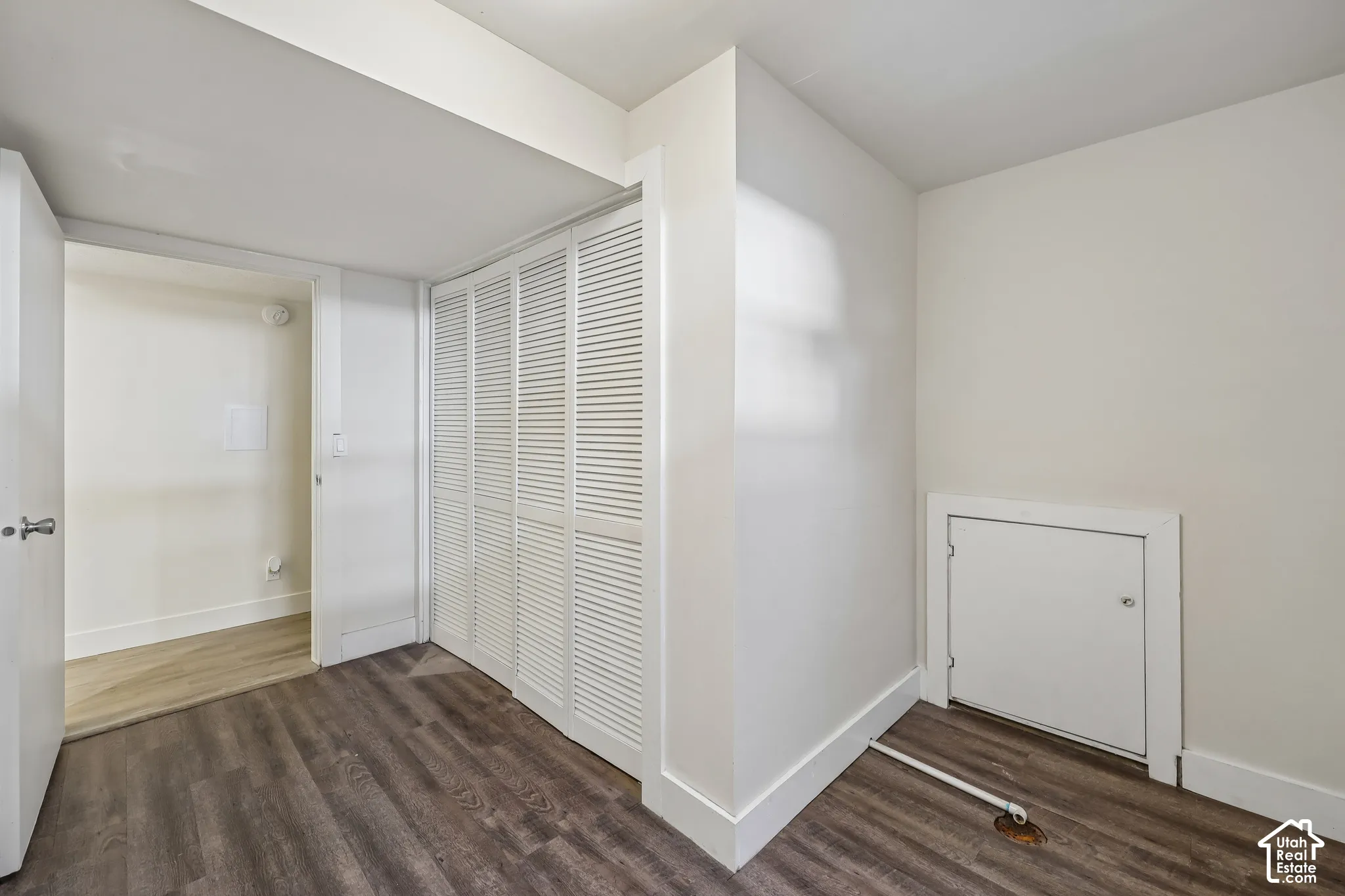 Wood-finish flooring with white baseboards, louvered bi-fold doors, and a built-in wall panel