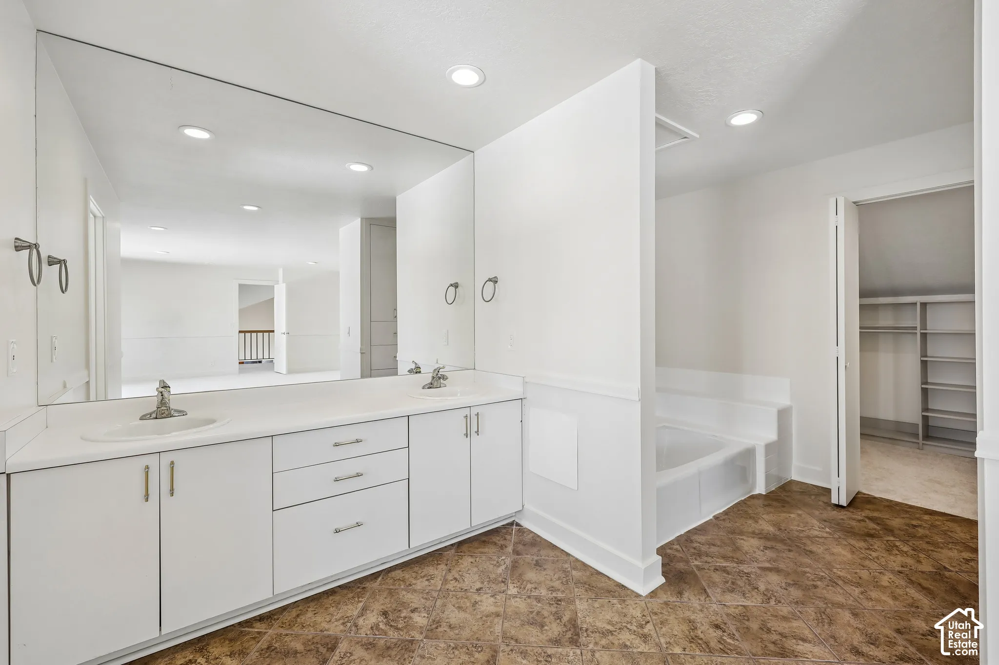 Dual vanity with integrated sinks, full-width mirror, recessed lighting, built-in bathtub, and closet with shelving