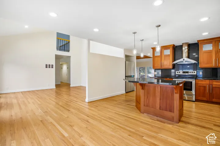 Hardwood flooring, kitchen island with dark countertop, stainless steel appliances, recessed lighting, and pendant lighting